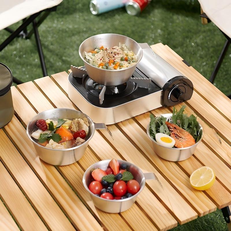 Camping cookware set with hot food on a folding table at an outdoor campsite
