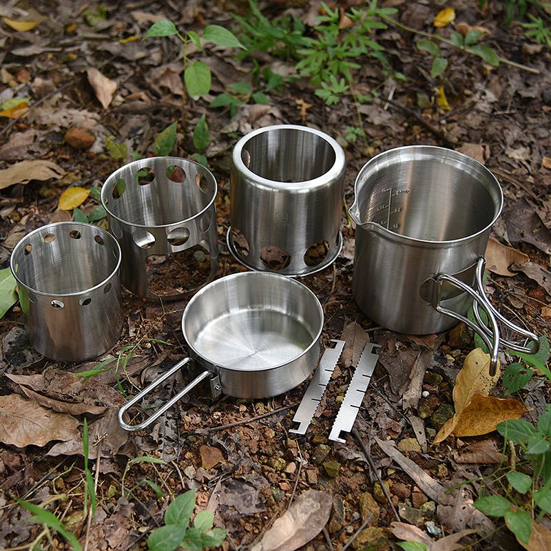 Stainless steel wood burning camp stove with fire, cooking pot and pan on forest floor